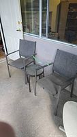 Two steel mesh patio chairs and round glass-top table on patio