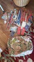 Overview of assorted knitting needles, crochet hooks, zippers, sewing needles laid out on floor alongside floral tote