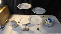 Full lot showing both pitchers, shakers on wood base, plate stand with four plates