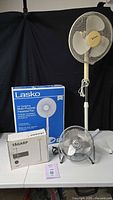 Full lot showing all boxed and assembled items: Lasko fan box, IKEA Tagarp lamp box, Massey desk fan, Hawaiian Breeze pedestal fan