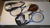 Group shot of four racquets, three covers and baseball on table