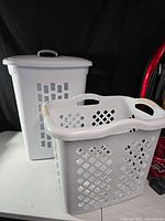 Two white plastic laundry baskets, one tall hamper with lid, one open basket