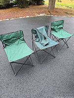 Three green folding chairs displayed on pavement