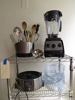 Overall lot on wire rack showing Vitamix blender, utensil holder with utensils, Breville steamer base, canning funnel and clear steam bowls