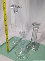 Front view of three glass candlesticks with tape measure showing height