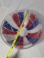 Top view showing segmented clear plastic bowl filled with red, white, blue beads with tape measure across diameter