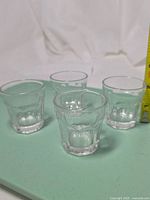 Four clear IKEA shot glasses on green surface showing shape and height
