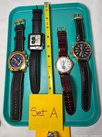 Front view of four Invicta watches on tray with measuring tape for scale