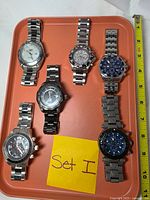 Top view of all six Invicta watches on tray with measuring tape