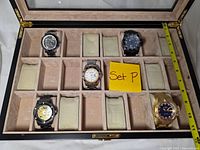 Open case showing five watches in separate compartments and tape measure for scale