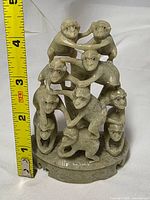 Front view of green soapstone monkey pile figurine beside tape measure showing height