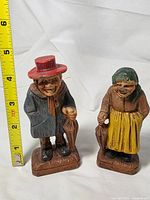 Front view of two Syroco figurines with tape for scale