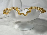 Side profile of pedestal bowl showing gold-edged ruffle rim and white milk glass body