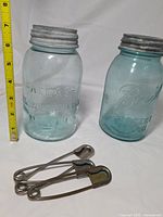 Atlas and Ball mason jars with three oversized safety pins, measuring tape for scale