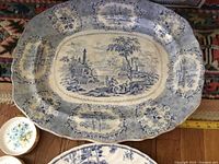 Overall view of large scenic blue toile platter with gold trim alongside other plates