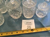 Three crystal jars with lids displayed next to measuring tape