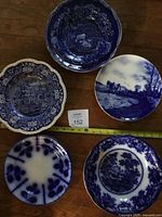Group of six blue-and-white plates arranged on floor with measuring tape