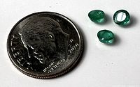 Three emeralds beside U.S. dime for scale