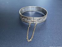 Full view of hinged sterling silver bangle with gold trim and safety chain