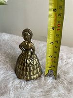 Front view of brass lady bell next to tape measure showing height