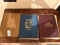 Three volumes laid on table showing covers: brown, blue, maroon