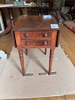 Full view of mahogany drop-leaf side table with drawers and turned legs
