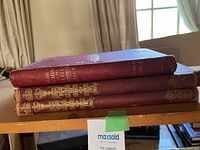 Three red cloth antique books stacked showing gilt spines and wear