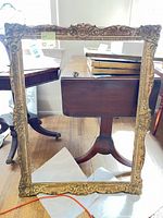 Full view of ornate gold frame leaning against table