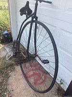 Full view of high-wheel bicycle leaning against garage door