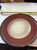 Full view of maroon and cream Susie Cooper plate with silver rim, tape measure showing size