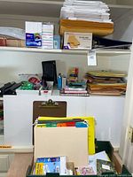 Shelved office supplies including envelopes, binders, notebooks, calculator