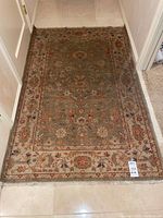 Full view of muted green floral rug showing overall pattern and fringe