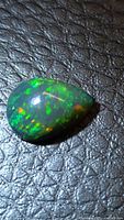 Pear-shaped black opal on textured surface showing play-of-color