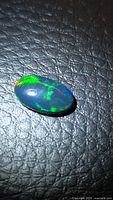 Oval black opal on textured background showing green and blue flashes
