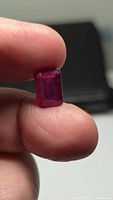 Emerald-cut ruby held between fingers, showing size and colour