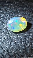 Faceted oval opal showing multicolour flashes on black textured surface