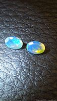 Pair of oval faceted opals showing color play on black textured background