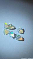 Six faceted triangular opals on neutral background displaying play-of-color
