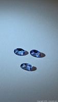 Three oval blue tanzanite gemstones on neutral background