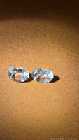 Two oval light blue faceted gemstones on brown background