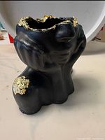 Front view of black abstract bust-shaped jewelry box with gold leaf detailing