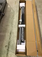 Tripod projector screen in open cardboard box with foam end caps and wrap