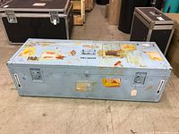Full front view of light blue metal shipping trunk with stickers and recessed hardware