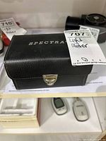 Closed black leatherette case labelled Spectra with lot tag visible