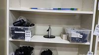 Shelf showing two bins filled with black brackets/adapters and a silver tabletop stand mount