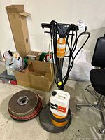 TASKI burnisher with cord, sprayer on handle, cleaner jug on base, pads and boxes nearby