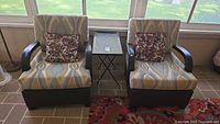 Two patio armchairs with cushions, pillows, and folding side table