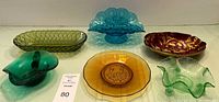 Group photo showing six glass pieces: green oblong dish, teal pedestal dish, red/gold bowl, green ashtray, amber plate, pale green candy dish