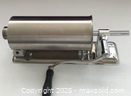 Side view of stainless steel horizontal sausage stuffer on base plate, crank handle visible