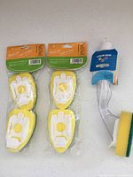Front view of dish wand and two sealed 2-packs of replacement sponge heads